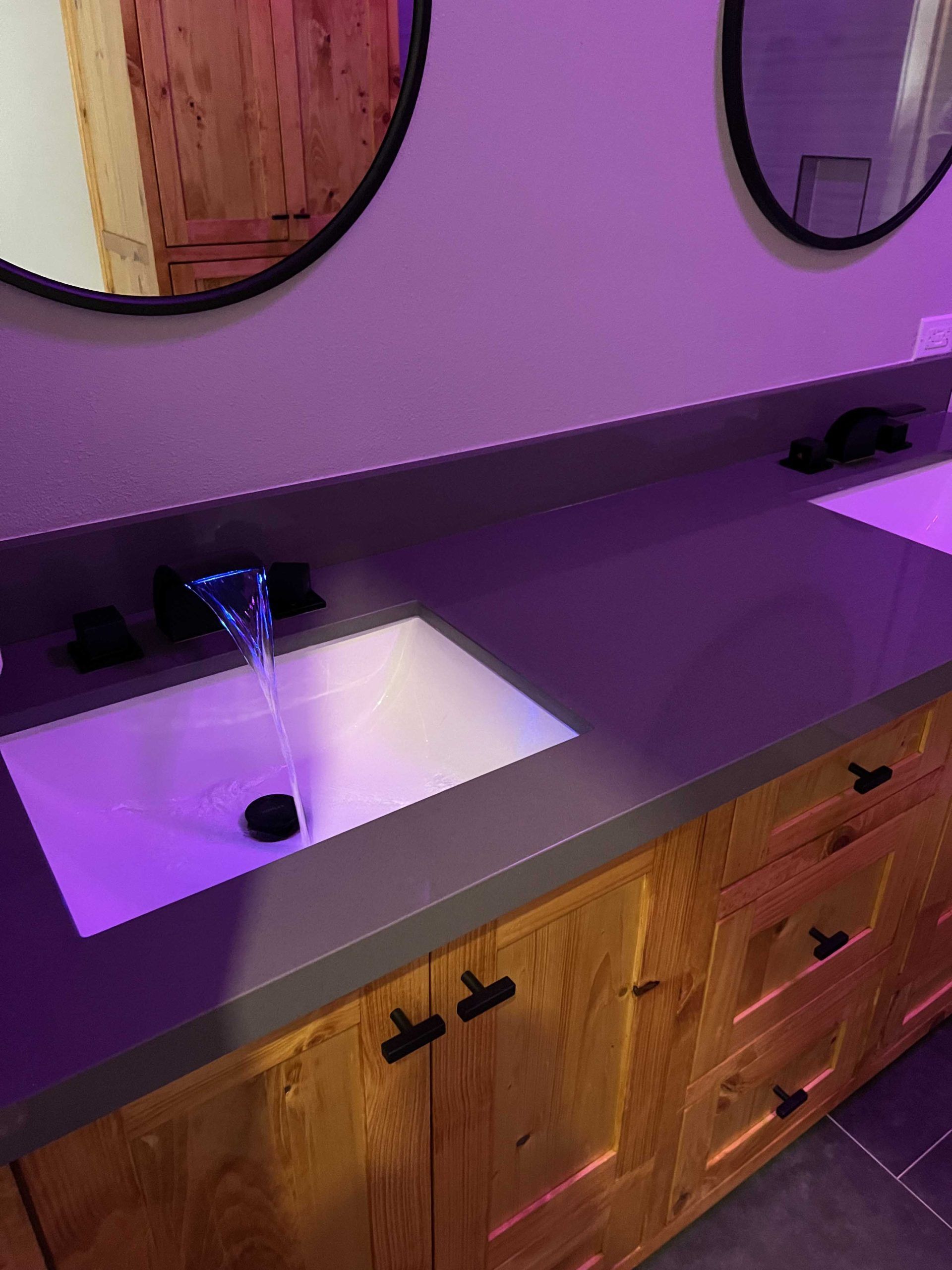 Bathroom vanity with wood cabinets, dark countertop, and rectangular sink. 