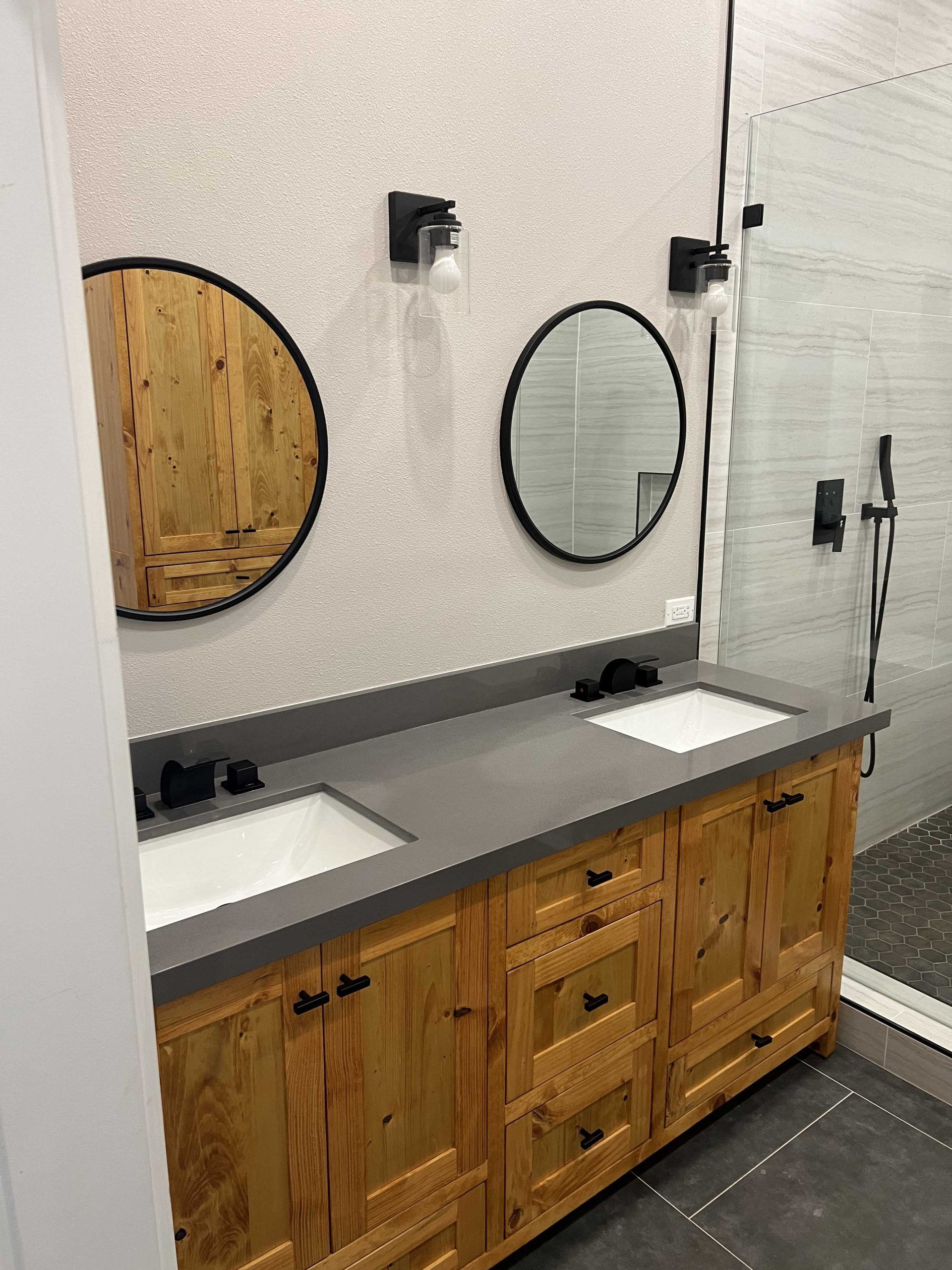 Bathroom with wood vanity, two round mirrors, and a shower with gray tile.