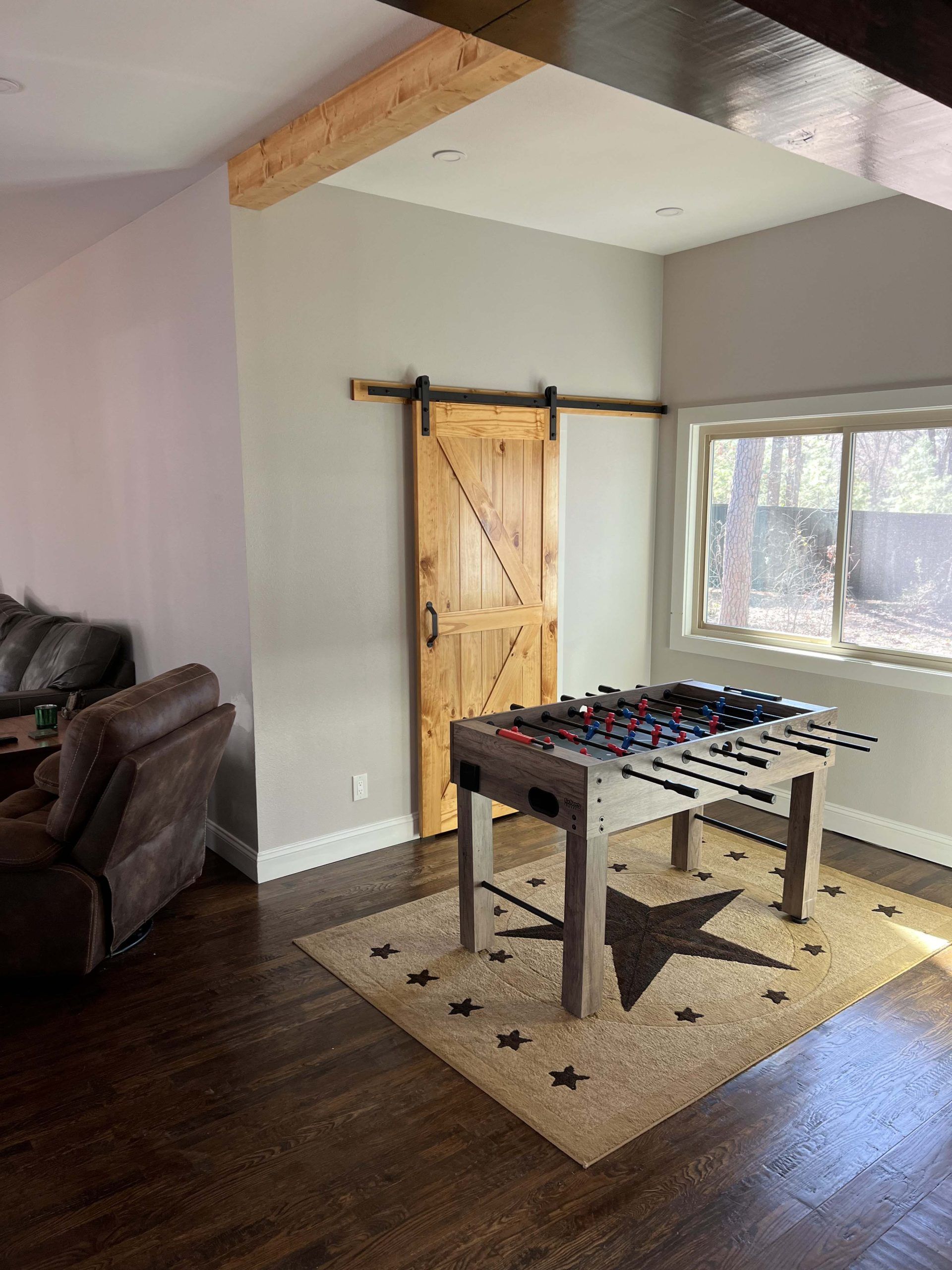 Foosball table on a star rug in a room with a barn door and a window.