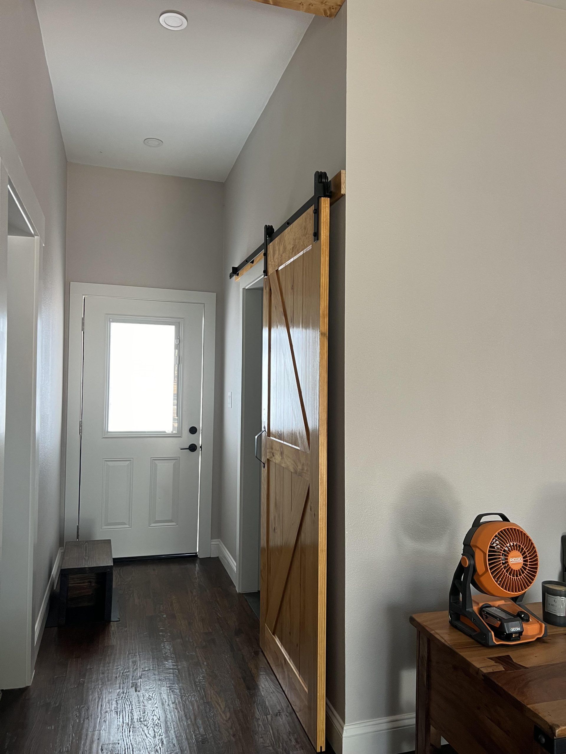 Hallway with a wooden sliding door, white door, and a table with a fan.