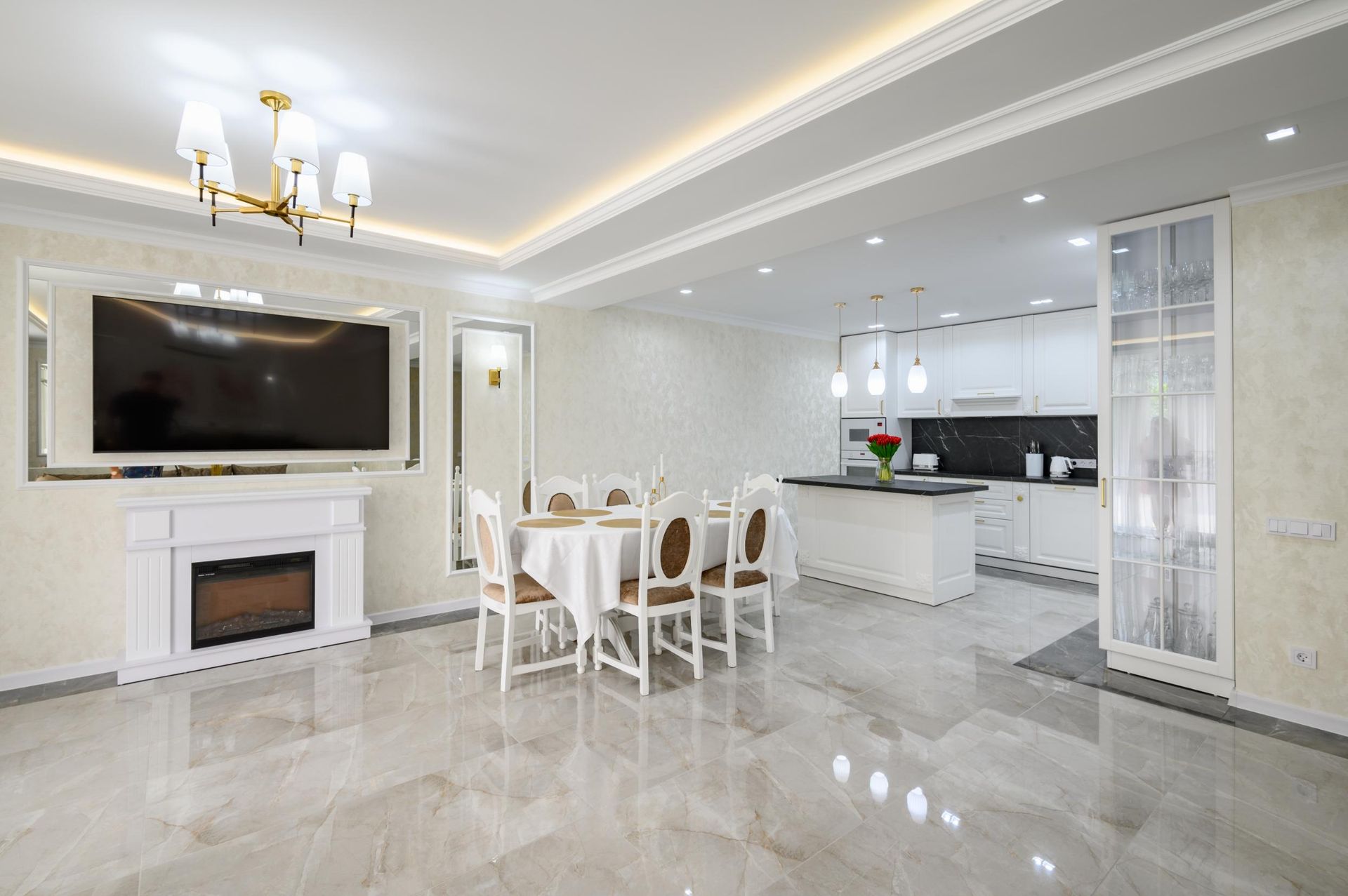 Spacious open-concept kitchen and dining area with white cabinets, a large TV, and marble flooring.