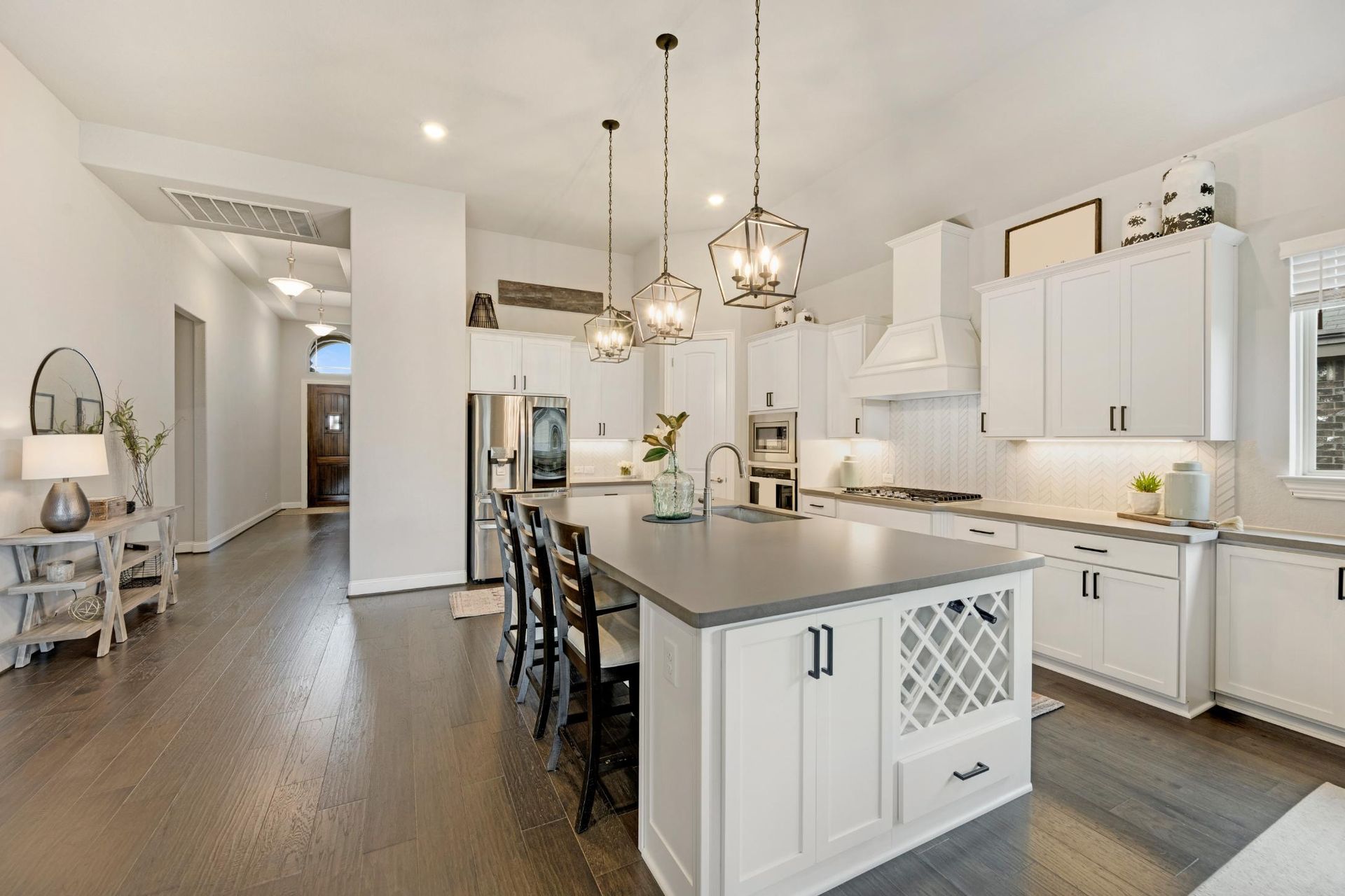 Modern white kitchen with island, pendant lights, cabinets, and dark wood floors.