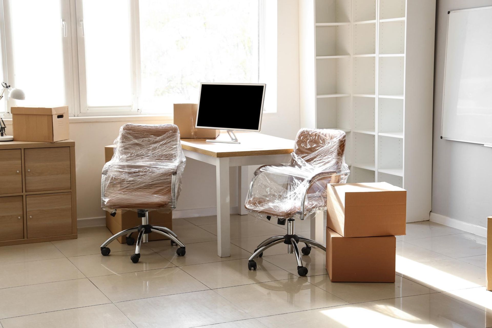 Office with boxes, chairs wrapped in plastic, and a computer on a desk, possibly preparing for a move.