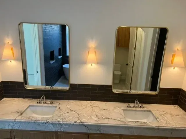 Two vanity mirrors with gold frames, sconces, and sinks on a marble countertop in a bathroom.