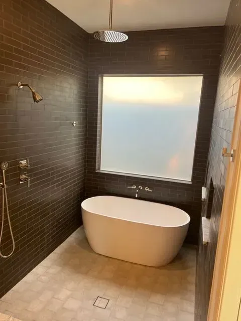 Modern bathroom with a white tub, dark brown tiled walls, and a frosted window.