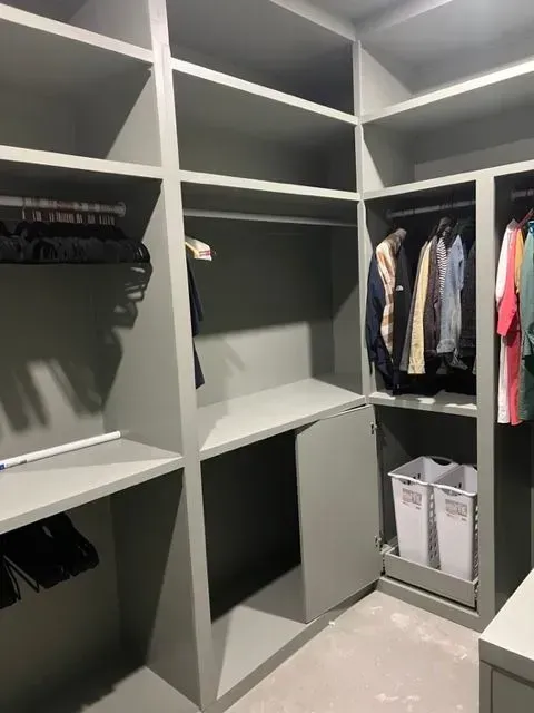 Gray walk-in closet with shelves and hanging rods; a cabinet door is open, and clothes and laundry baskets are visible.