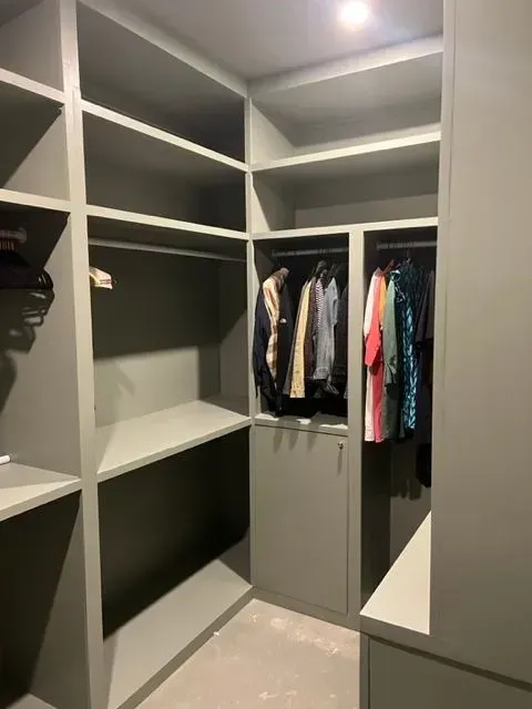 Gray walk-in closet with shelves and hanging rods; clothes are hanging.