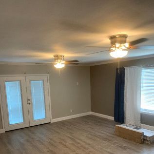 Interior of a room with two ceiling fans, a window, and double doors; neutral walls and laminate flooring.