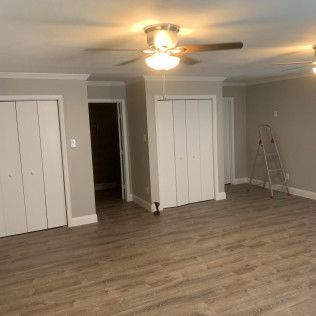 Interior of a room with light brown wood-like flooring, white doors and trim, and gray walls. A ceiling fan is visible.