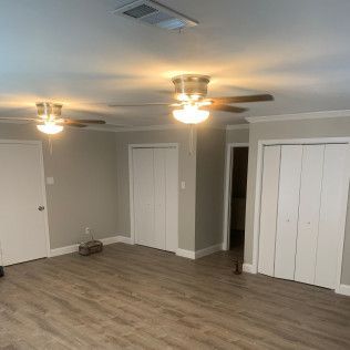 Room with two ceiling fans, white doors, gray walls, and wood-look flooring.