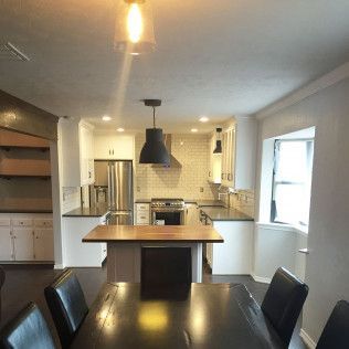 Kitchen and dining area with island, dark pendant lights, white cabinets, stainless steel appliances, and wood table.