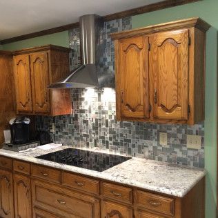 Kitchen with wooden cabinets, granite countertops, tile backsplash, and stainless steel range hood.