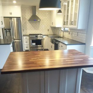 Modern kitchen with stainless steel appliances, white cabinets, subway tile backsplash, and butcher block island.