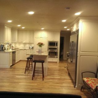 Well-lit kitchen with white cabinets, wood floor, stainless steel appliances, and a central island with stools.