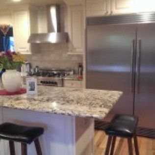 Kitchen island with granite countertop, stainless steel refrigerator and stools.