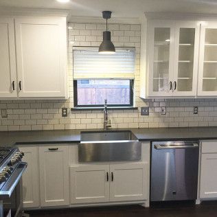 White kitchen with stainless steel sink and appliances; dark countertops, subway tile backsplash.