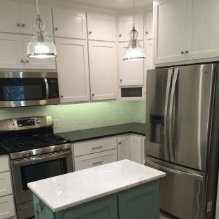 Kitchen with white cabinets, stainless steel appliances, green island, and glass pendant lights.