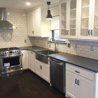 White kitchen with subway tile backsplash, stainless steel appliances, dark countertops, and dark wood floors.