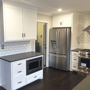 White kitchen with dark countertops, stainless steel appliances, and subway tile backsplash.