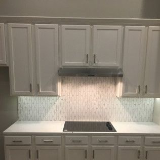 White kitchen cabinets with matching countertops, backsplash, and cooktop.