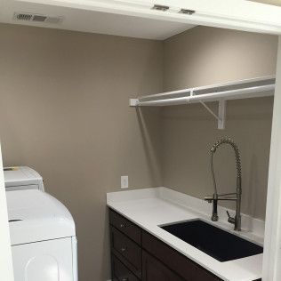 Laundry room with washer, sink, countertop, cabinets, and shelf. Beige walls and white trim.