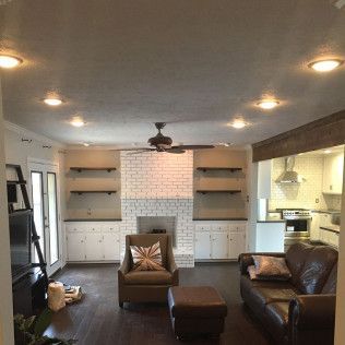 Living room with white brick fireplace, built-in shelves, brown leather couch, and dark wood floors.