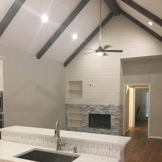 Interior view of a modern kitchen and living room with a fireplace and vaulted ceiling with dark wooden beams.