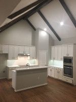 White kitchen with light wood floors, gray island, white cabinets, and dark beams in the ceiling.