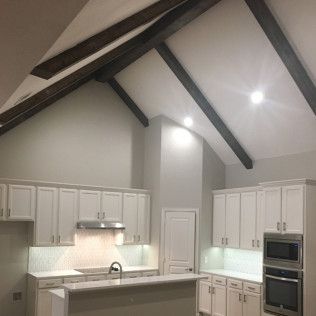 White kitchen with vaulted ceiling and dark wood beams.