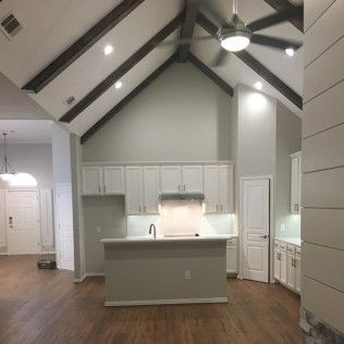 Interior kitchen with vaulted ceiling, white cabinets, island, and wood beams.