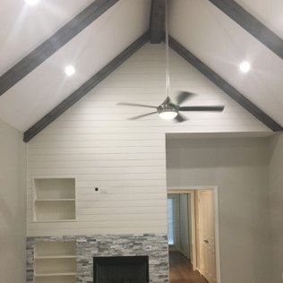 Vaulted ceiling with gray beams, shiplap wall, stone fireplace, and a ceiling fan.