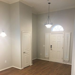 Empty entry hall with hardwood floors, white doors, and light gray walls.