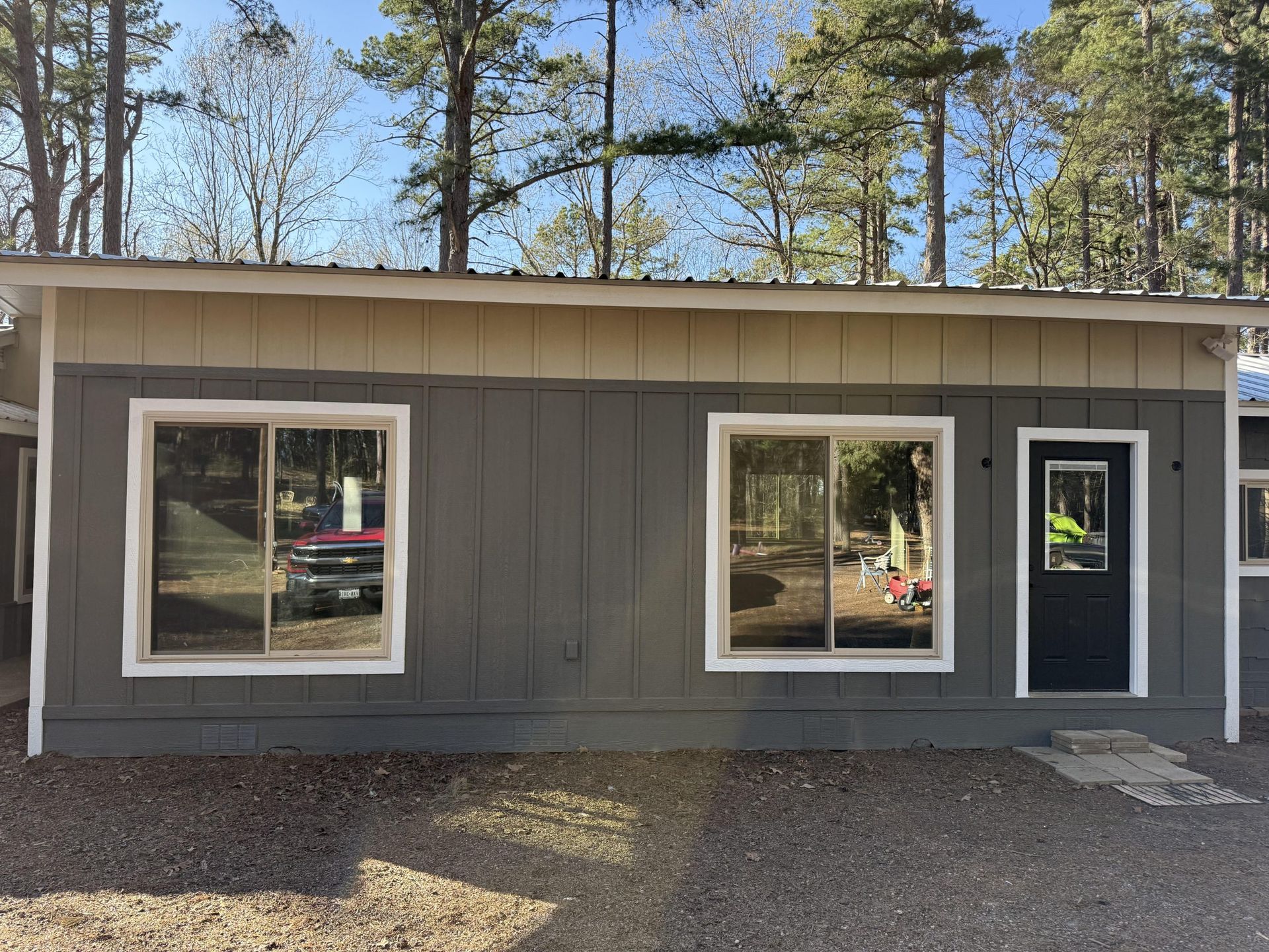 Gray building with windows and a black door; set in a wooded area.