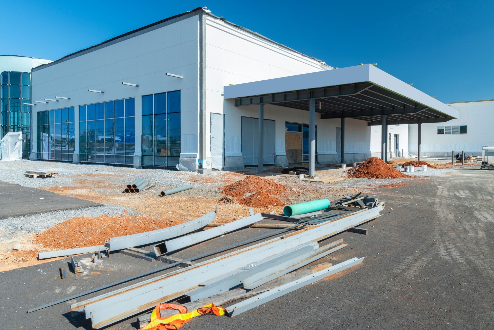 Building under construction with glass windows and a covered entrance. Construction materials on ground.