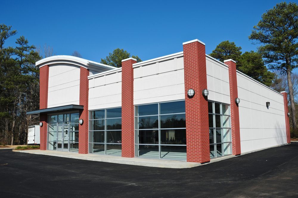 Modern commercial building with white walls, red brick columns, and large windows under a blue sky.