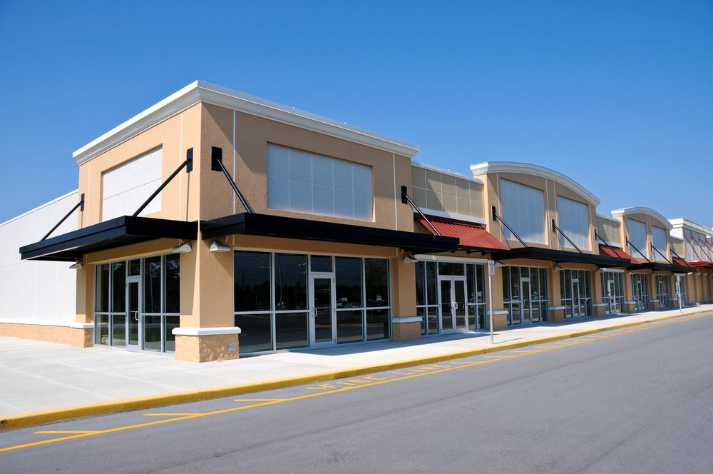 Row of vacant, beige storefronts with awnings, sidewalk, and blue sky.
