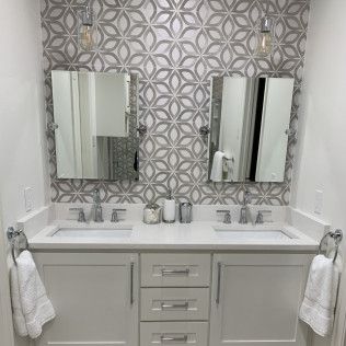 Bathroom vanity with two sinks, mirrors, patterned tile, and light fixtures.