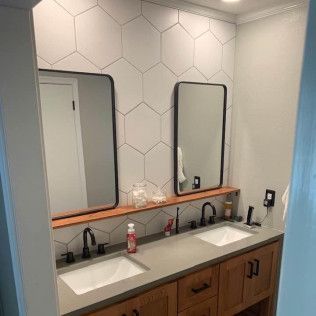 Bathroom with two sinks, mirrors, and wooden vanity. White hexagon tile wall, black fixtures, and a wooden shelf.