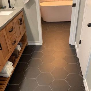 Bathroom with dark hexagonal floor tiles, wooden vanity, and a white soaking tub.