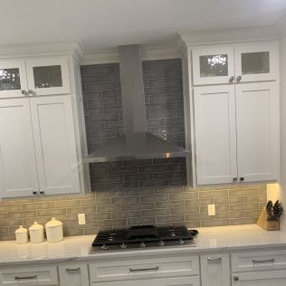 Kitchen with white cabinets, stainless steel range hood, gray backsplash, and gas stovetop.