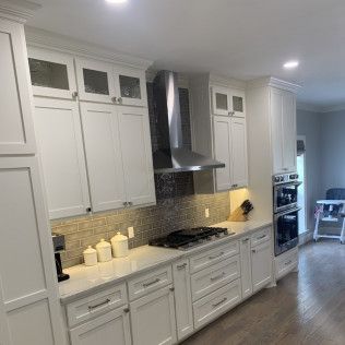 White kitchen with stainless steel range hood, cabinetry, and stovetop.