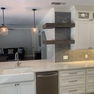 Modern kitchen with white cabinets, farmhouse sink, and open shelves with a dark gray tiled backsplash.