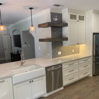 Modern kitchen with white cabinets, farmhouse sink, stainless steel appliances, and floating shelves.