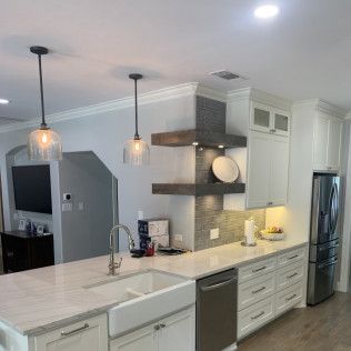 Modern white kitchen with island, sink, and stainless steel appliances.