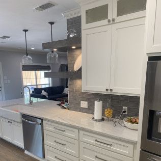 Modern kitchen with white cabinets, stainless steel appliances, and gray backsplash.