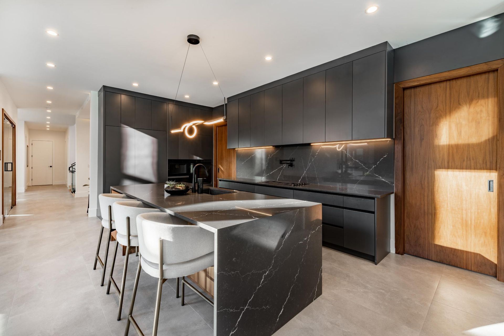 Modern kitchen with gray cabinets, black marble countertops, and a large island with bar stools.