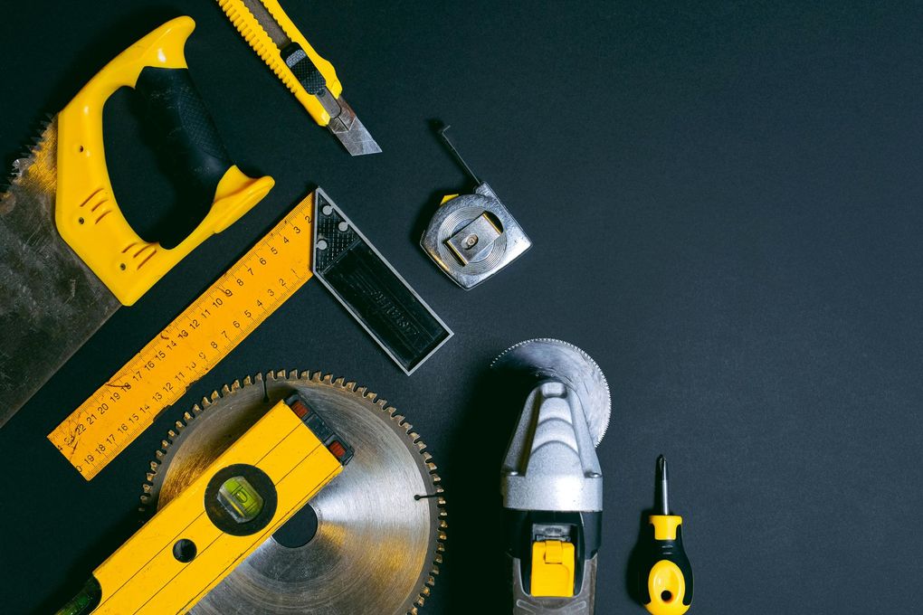 Yellow and black construction tools on a black surface: saw, level, angle grinder, and more.