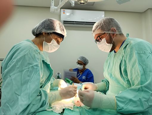 Cirurgião em sala de cirurgia, usando máscara e luvas, utilizando instrumentos no paciente. Ambiente cirúrgico.