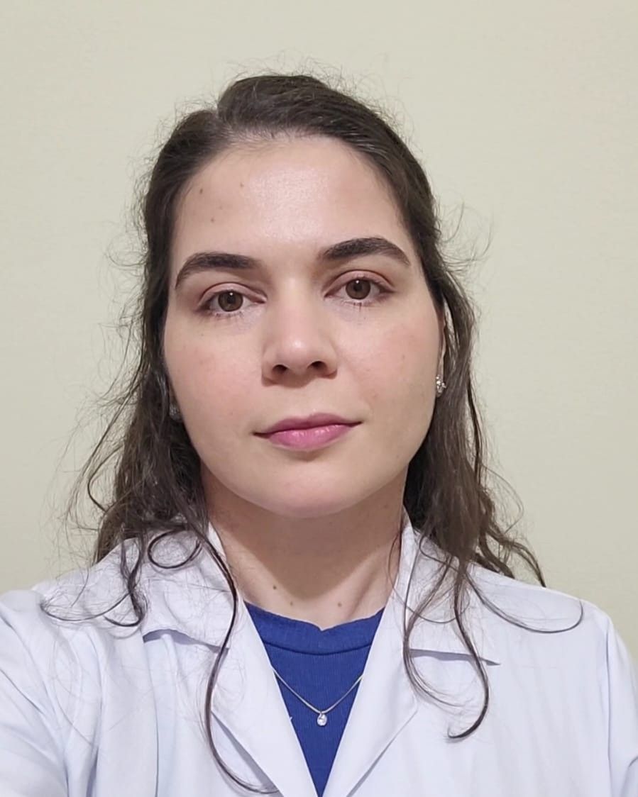 Mulher vestindo uniforme cirúrgico verde-azulado e estetoscópio, braços cruzados, sorrindo.