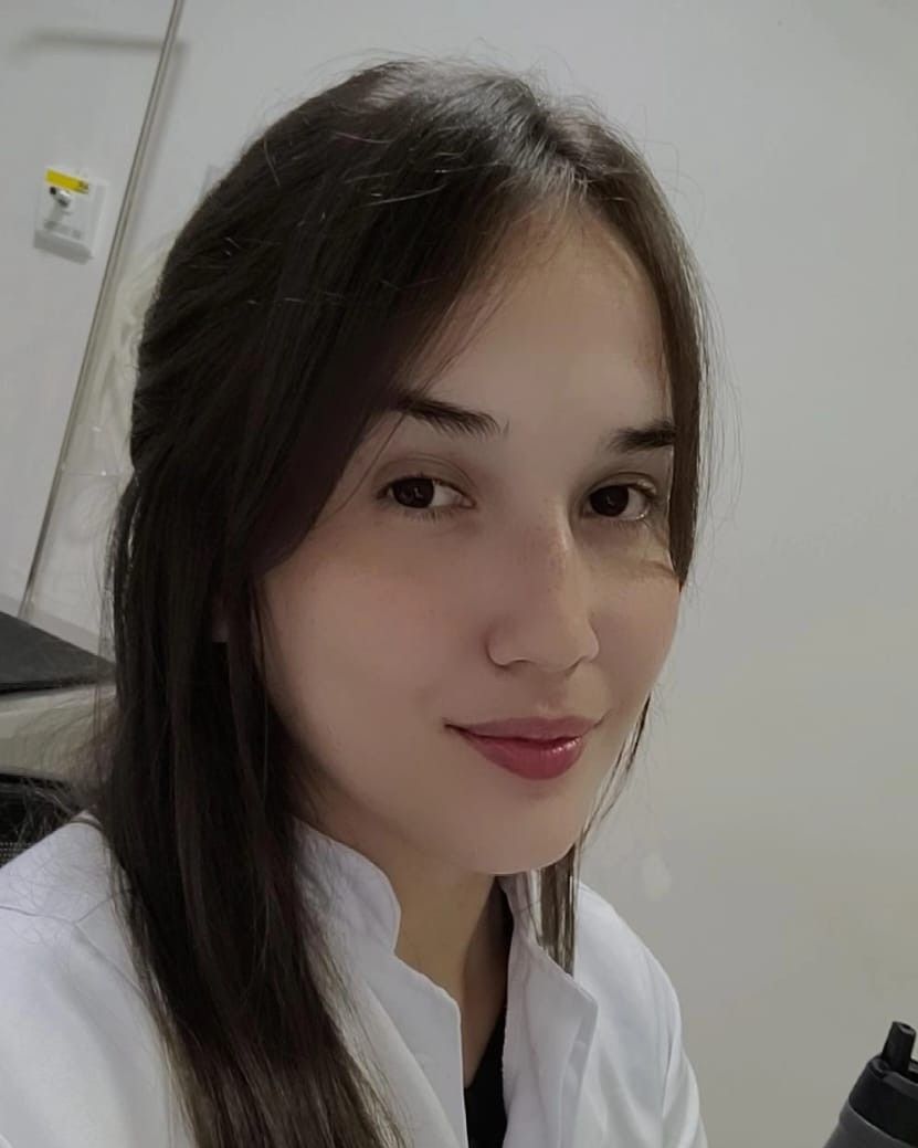 Mulher vestindo uniforme cirúrgico verde-azulado e estetoscópio, braços cruzados, sorrindo.